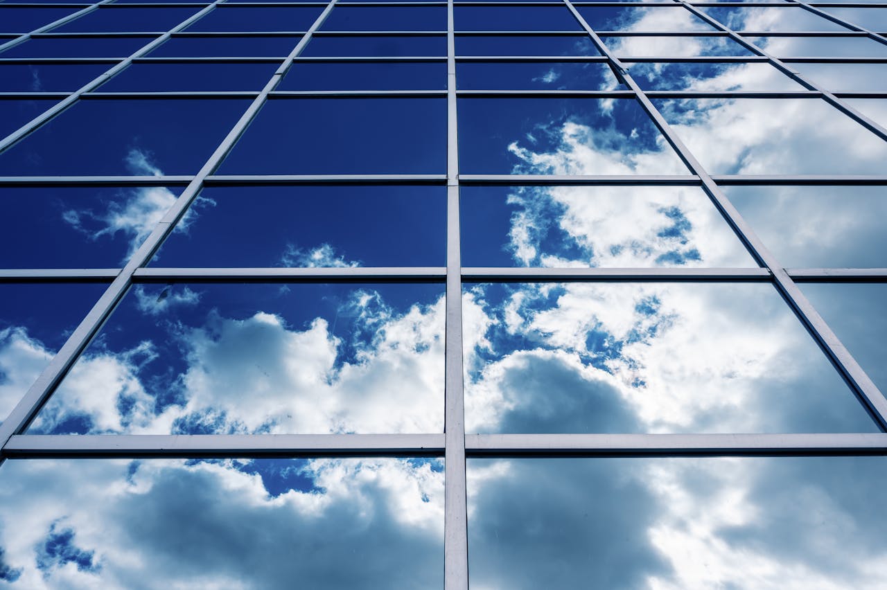 Symmetrical glass facade of a modern building reflecting a bright, cloudy sky.