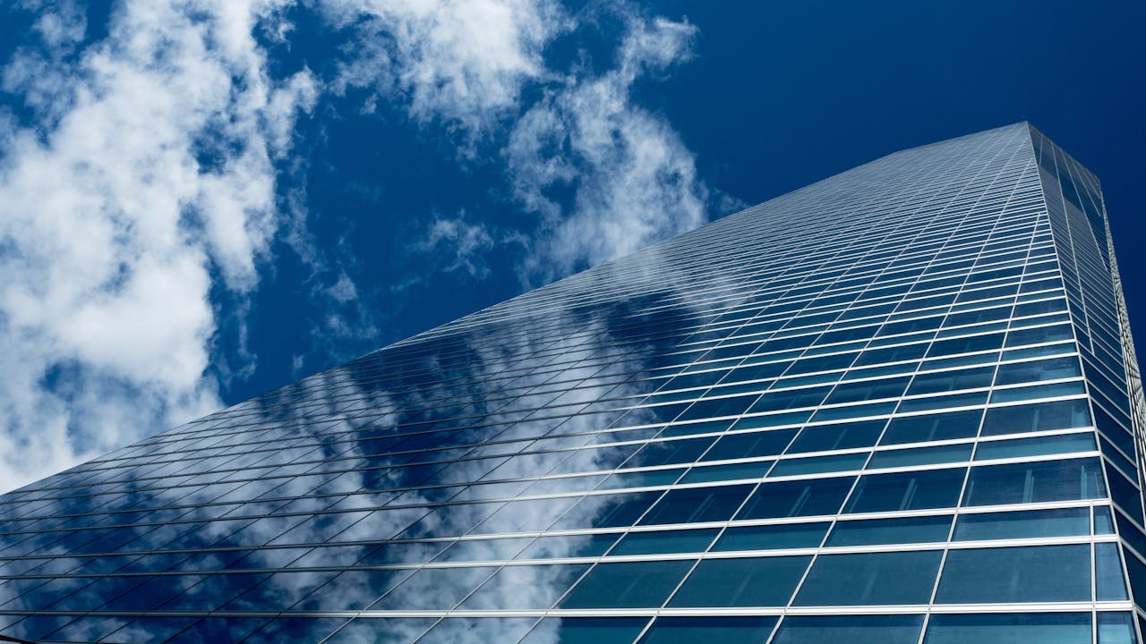 Low-angle view of a modern skyscraper with reflective glass windows against a blue sky.