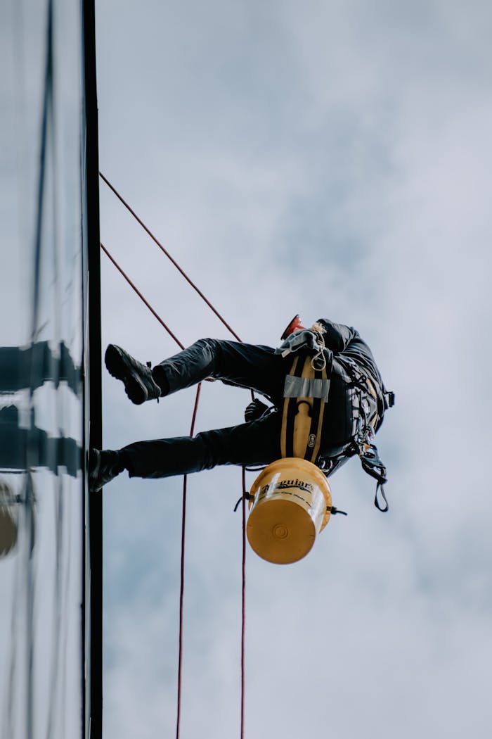 High-angle view of a window washer scaling a building facade with cleaning gear and ropes.